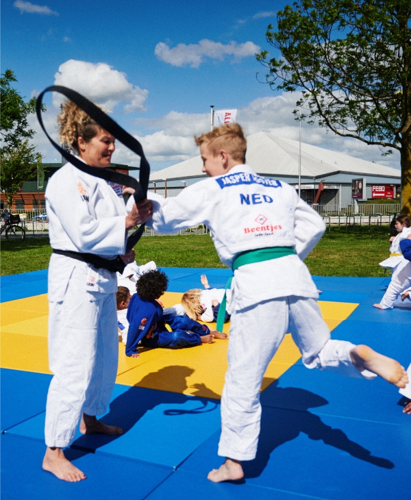 Sfeerbeeld: judoleraar en jonge judoka oefenen met een judoband op de mat